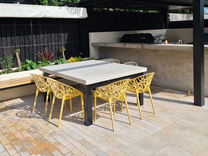 rectangular outdoor table made from lightweight concrete and surrounded by yellow painted chairs