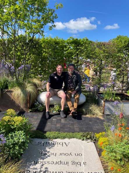 Richard Bickler and Rick Ford sit side by side on a stone bench in the very pretty Abigails Garden created for the RHS Malvern Show