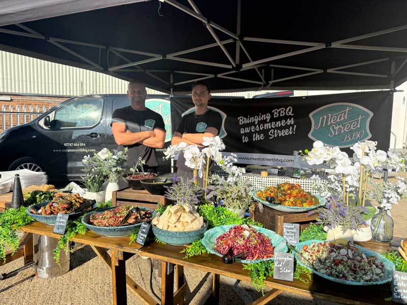 two gentlemen from Meat Street mobile caterers dressed in black and standing behind a table full of delicious looking food
