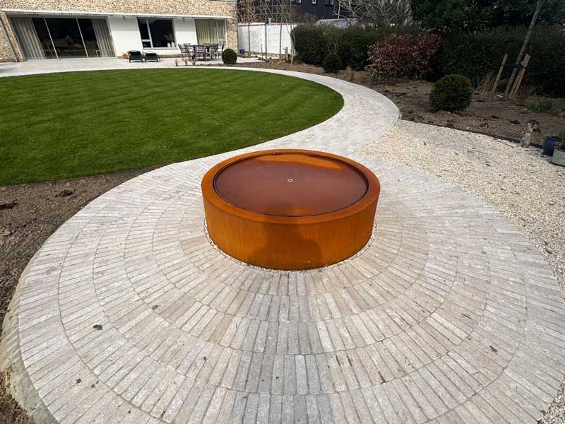 corten steel water feature placed upon a circular patio created using limestone slim setts from Arbour Landscape Solutions