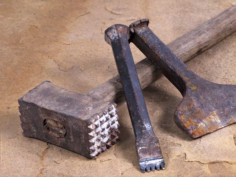 Stonemasons tools. A bush hammer and a chisel lie on a piece of sandstone