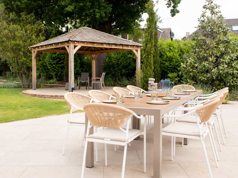 large porcelain patio dressed with table and chairs for 8 people and with views towards a victorian style timber pergola