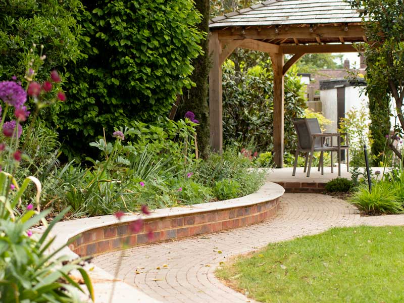 winding path alongside beautiful planting leads to a timber built pergola with a tiled roof