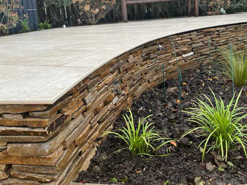 patio raised by approximately 20cm above a planting bed, riser is created using paddlestones for a dry stone wall effect