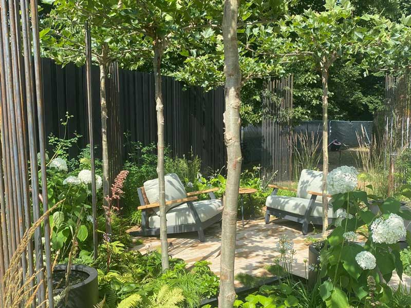 relaxing seating area for two people in a small garden with trees and woodland planting