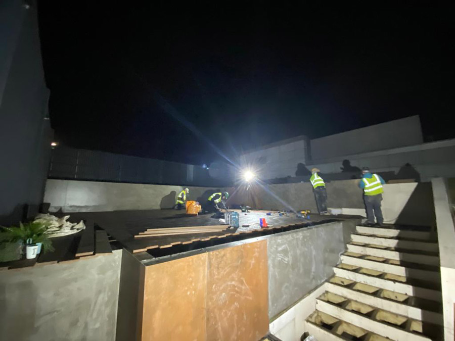 workmen installing decking boards by floodlights