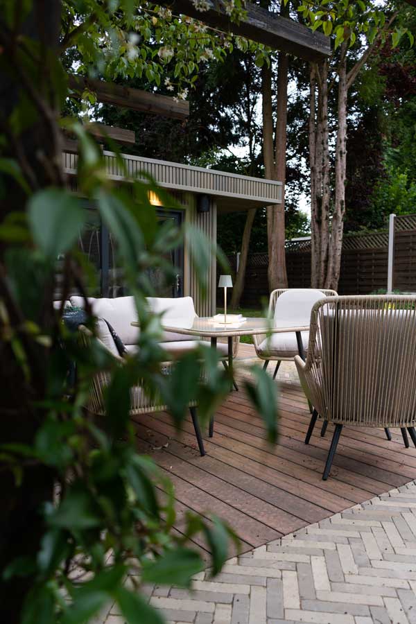 beautiful garden room beneath a large overhanging tree with comfortable garden sofas on the adjoining patio designed by Diana Behanaru