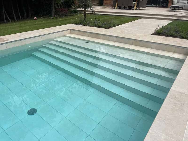 Jura beige porcelain pavers from Arbour Landscape Solutions surround an elegant outdoor swimming pool