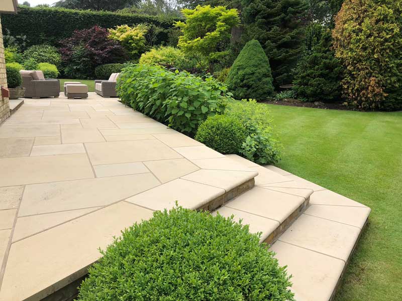 beautiful buff coloured limestone patio with comfy seating and views across a lawned garden with mature shrubs