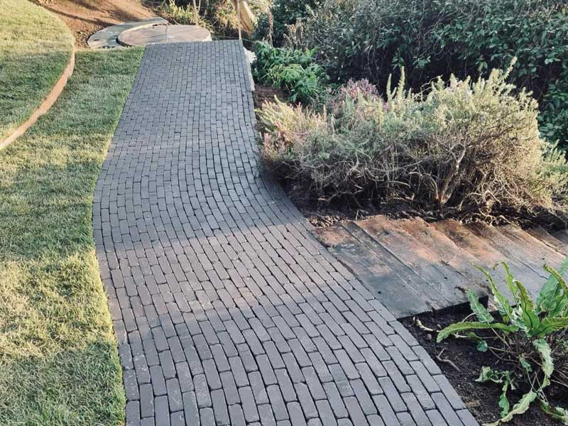 charcoal grey coloured clay pavers laid in a running bond pattern to create a snaking path in a coastal garden