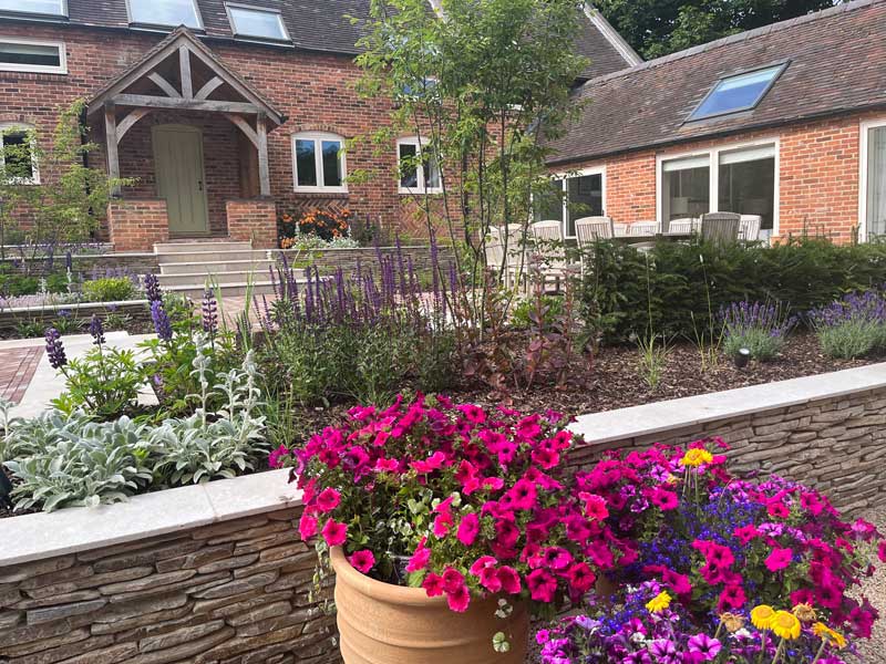 a planter full of hot pink petunias sitting in front of a paddlestone wall in a derbyshire farmhouse garden