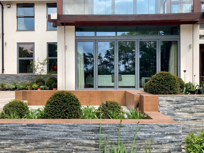 stylish garden for a large new build home with grey coloured retaining walls contrasting with planting