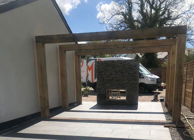 outdoor fireplace built from paddlestones nestling beneath a sturdy timber pergola