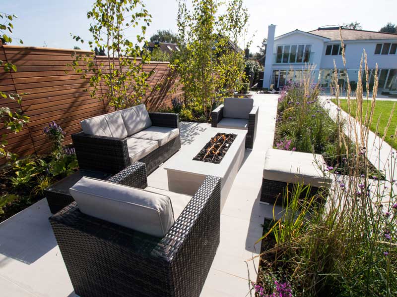 beautifully designed garden with seating area and firepit and views across a lawn and swimming pool 