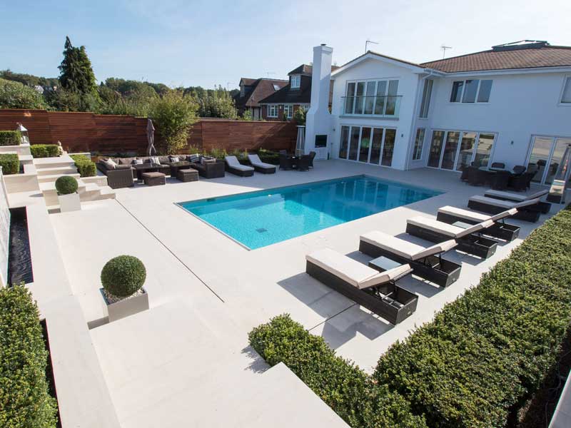 large garden with a swimming pool landscaped using pale coloured porcelain paving for pool surround and steps