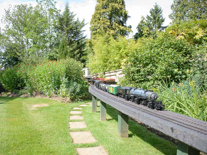 garden with steam locomotive on raised model railway track running between flower beds