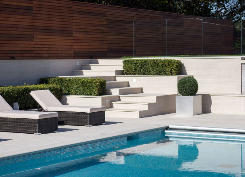 swimming pool with hard landscaping in white pavers and steps