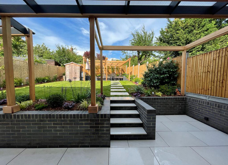 covered patio with timber pergola and glass roof. Views across the garden to a second timber pergola with seating area