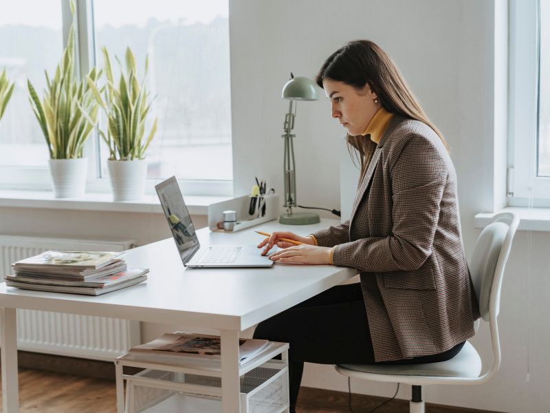 woman wearing tweed jacket working at a desk in a modern office with plants on the windowsill